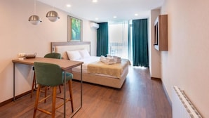 A hotel room with a bed, a desk, two chairs, a TV, and a window with curtains. - Rainbow Residence (Batumi)