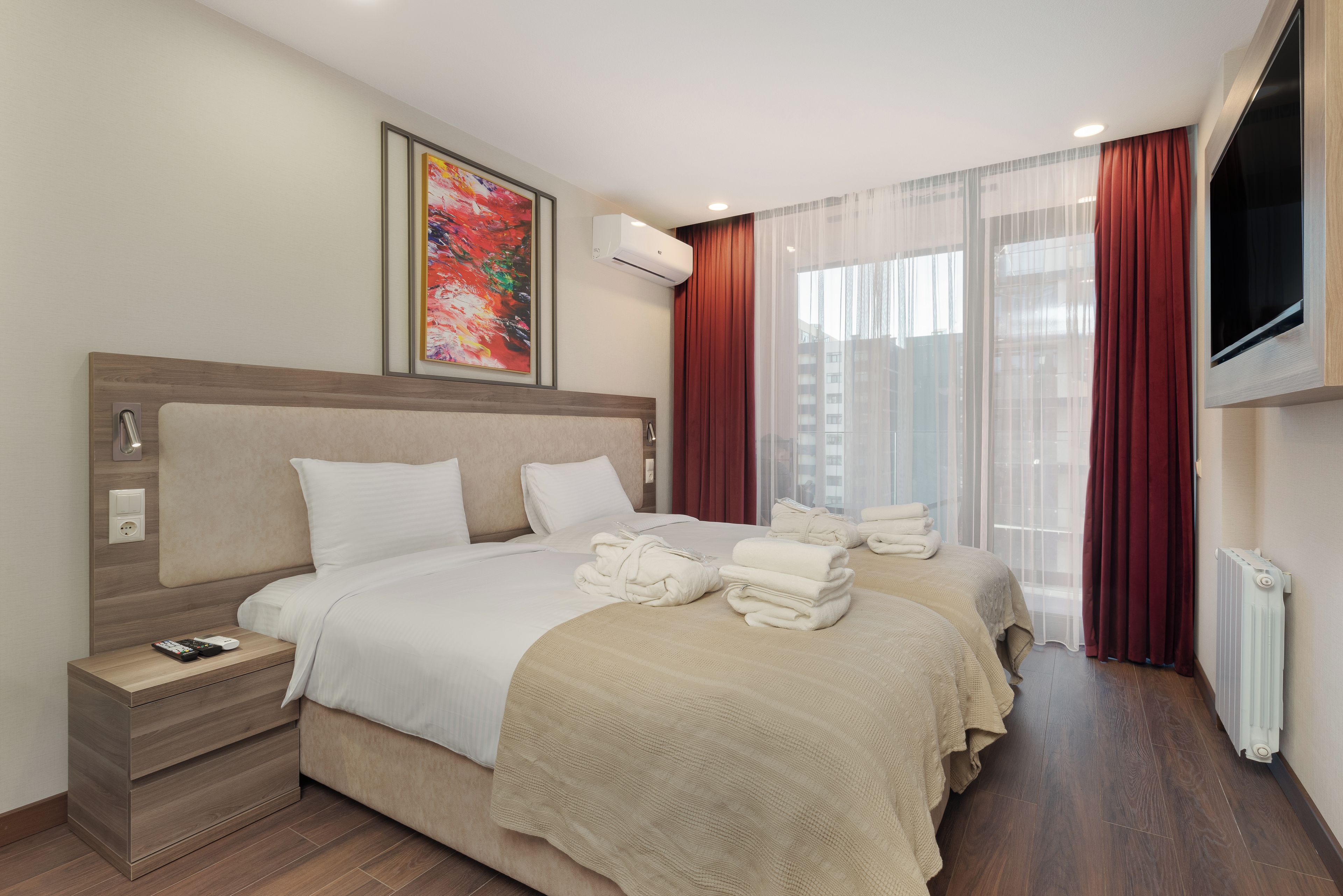 A hotel room with a large bed, a bedside table with a phone, a TV mounted on the wall, and a window with curtains.