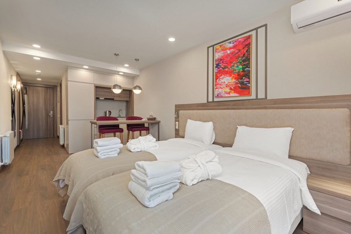 Ein Hotelzimmer mit zwei Betten, einem Schreibtisch, einem Stuhl und einem großen abstrakten Gemälde.