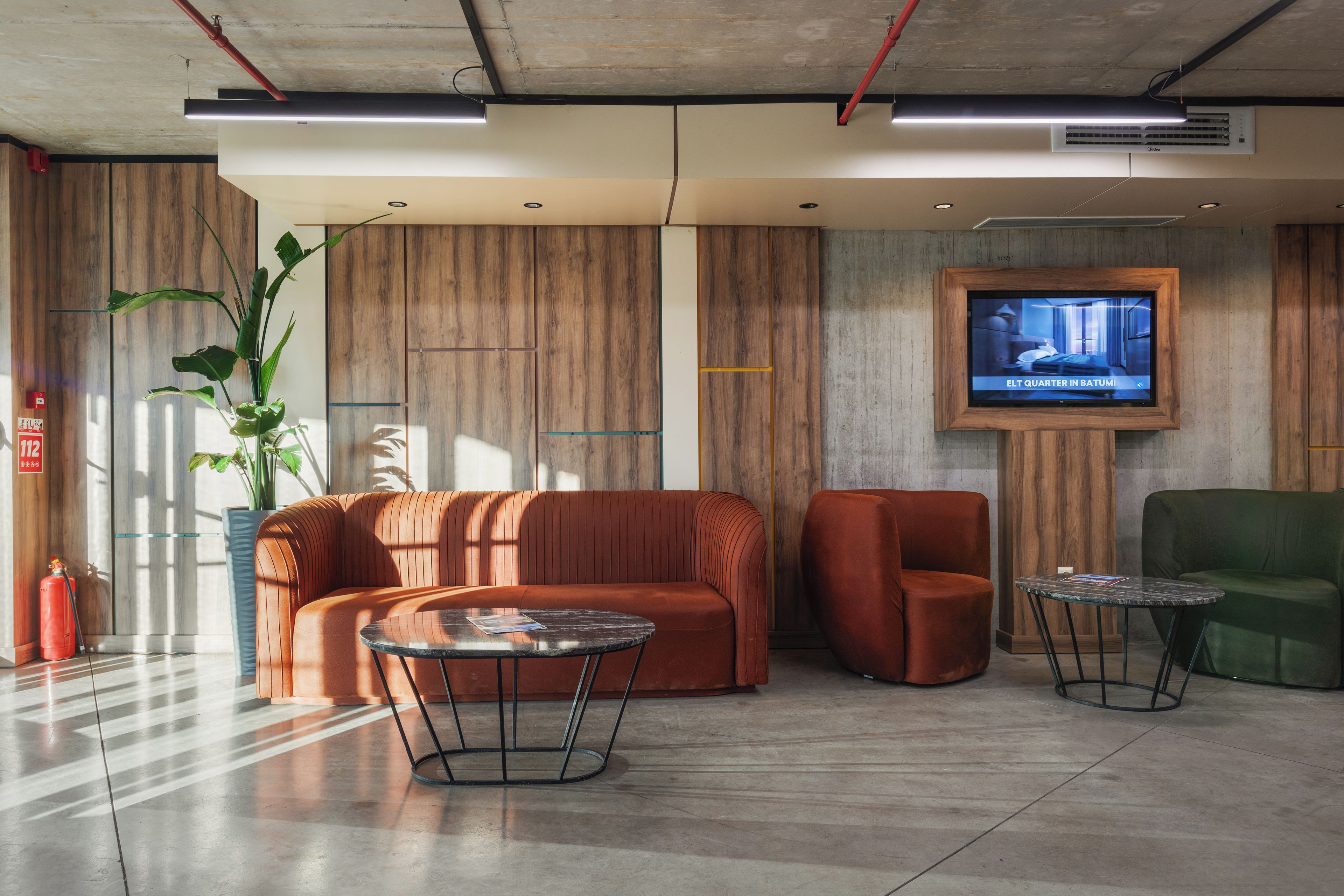 Eine moderne Lobby mit einem Ecksofa, zwei Sesseln, einem kleinen runden Tisch und einem an der Wand befestigten Fernseher.