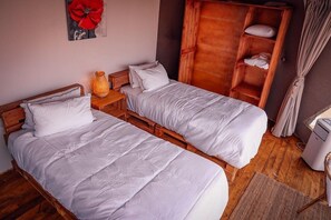 Twee eenpersoonsbedden met houten frames, een houten garderobe, een klein tafeltje met een lamp en een schilderij aan de muur.