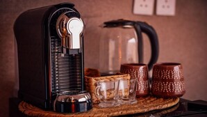 En kaffemaskine med et nøglehul, en krystal kande og to keramiske kopper på en vævet måtte.