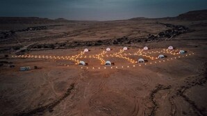 Et ørkenlandskab med flere kuppelformede telte arrangeret i en cirkel, forbundet af en lyskæde.