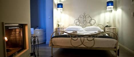 A bedroom with a metal bed frame, bedside lamps, a nightstand, and a fireplace.
