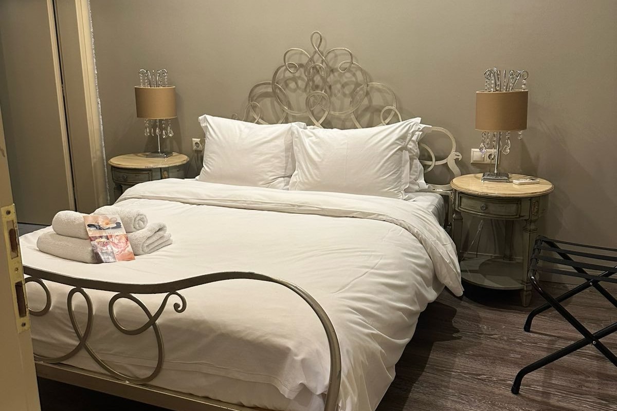 A neatly made bed with white linens, two bedside tables with lamps, and a wooden floor.