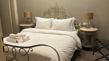 A neatly made bed with white linens, two bedside tables with lamps, and a wooden floor.