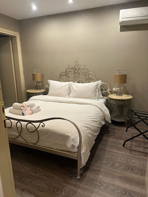 A neatly made bed with white linens, two bedside tables with lamps, and a wooden floor.