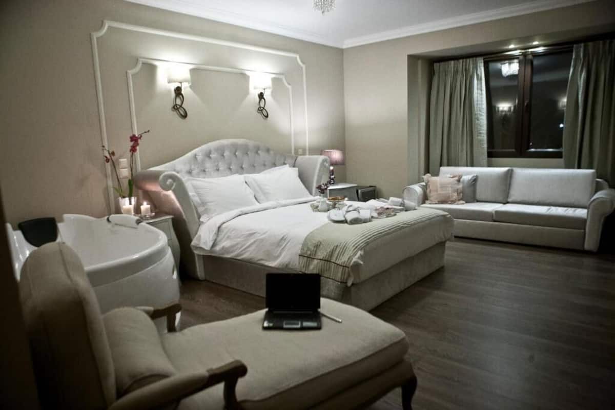 Habitación de hotel con una cama grande, un sofá, una silla, una computadora portátil y una mesita de noche con una lámpara.