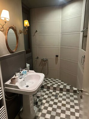 Un bagno con pavimento a scacchi, un lavandino con specchio e zona doccia.