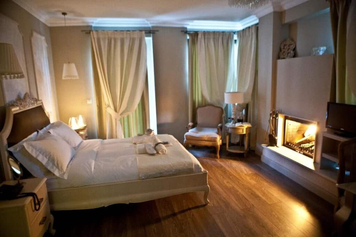 Una habitación de hotel con una cama, una silla, una mesita auxiliar, una lámpara y una chimenea.