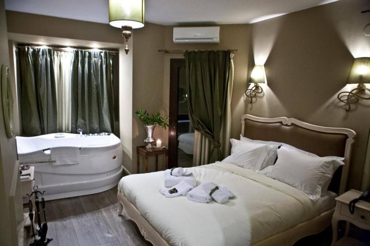 Habitación de hotel con una cama grande, una bañera separada, un tocador con espejo y dos lámparas de pared.