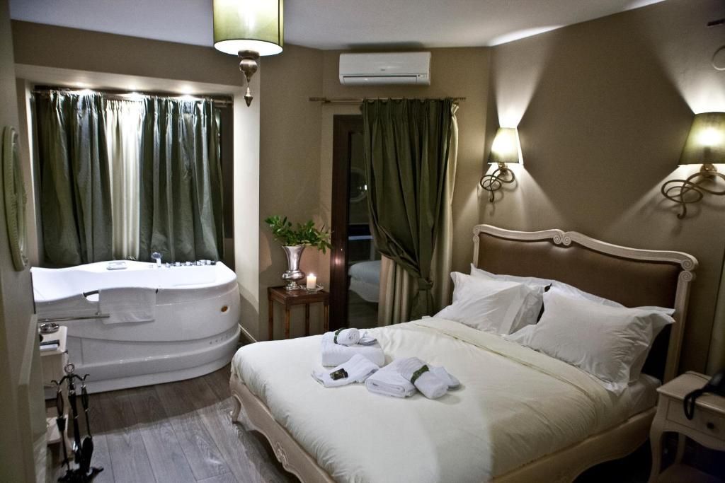 A hotel room with a large bed, a separate bathtub, a vanity with a mirror, and two wall-mounted lamps.