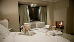 Una habitación de hotel con cama, sofá, chimenea y ventana con cortinas.