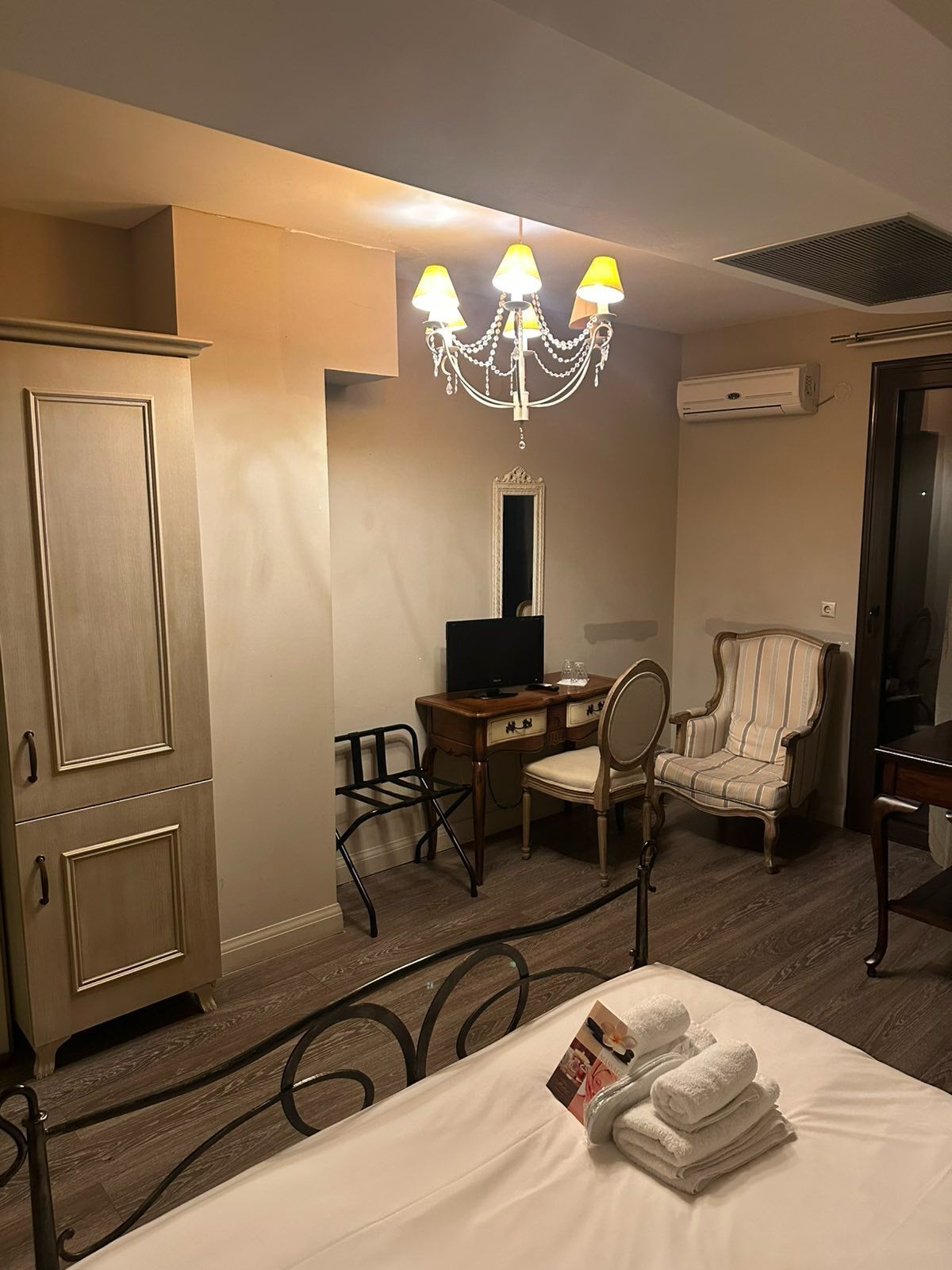 Une chambre d’hôtel comprenant un lit, un bureau avec un ordinateur, une chaise, une armoire et un lustre.