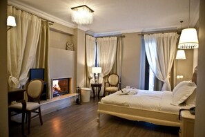 A hotel room with a bed, a television, a fireplace, and a desk with a chair. - Melies Boutique Hotel (Almopia)