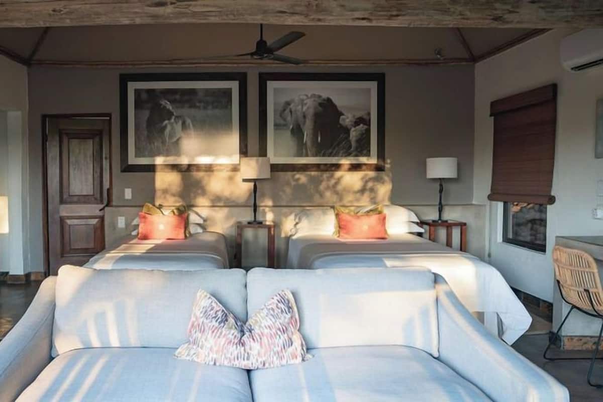 A hotel room with two beds, a ceiling fan, framed pictures on the wall, and a window with a view.