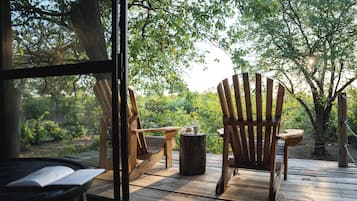 A wooden deck with two Adirondack chairs, a small table, and a rustic wooden stool.
