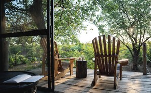 A wooden deck with two Adirondack chairs, a small table, and a rustic wooden stool. - Mashatu Lodge (Lentswelemoriti)