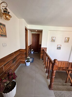 A hallway with wooden paneling, a staircase with wooden balusters, and potted plants. - The Berlin Cottage (Manali)