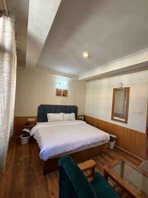 A bedroom with a bed, bedside tables, a mirror, a small table, and a chair. - The Berlin Cottage (Manali)