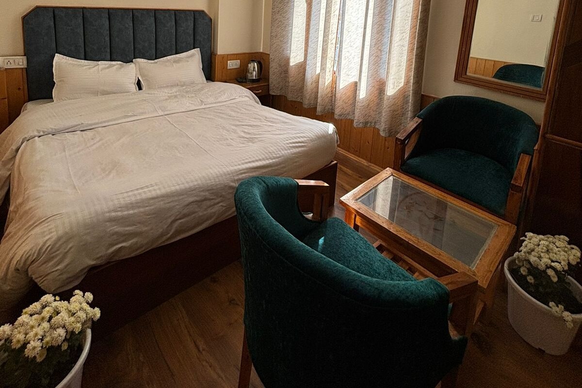 A hotel room with a bed, a desk, a chair, a potted plant, and a mirror.