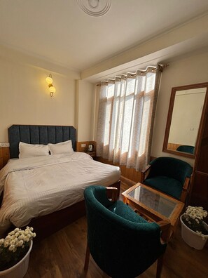 A hotel room with a bed, a desk, a chair, a potted plant, and a mirror. - The Berlin Cottage (Manali)