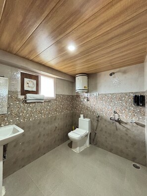 A bathroom with a toilet, sink, shower, and decorative wall tiles. - The Berlin Cottage (Manali)