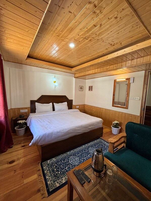 A wooden-paneled room with a bed, a sofa, a coffee table, and a mirror. - The Berlin Cottage (Manali)