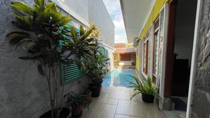 A narrow corridor with a tiled floor, potted plants, a small pool, and a building with a tiled roof and wooden doors. - Serene 2-bedroom villa with AC in welcoming Jogja (Jogja)