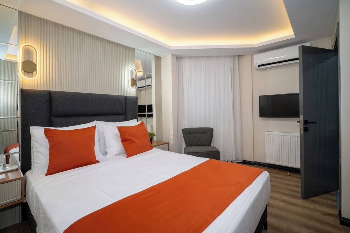 A hotel room with a large bed, a chair, a TV, and a door.