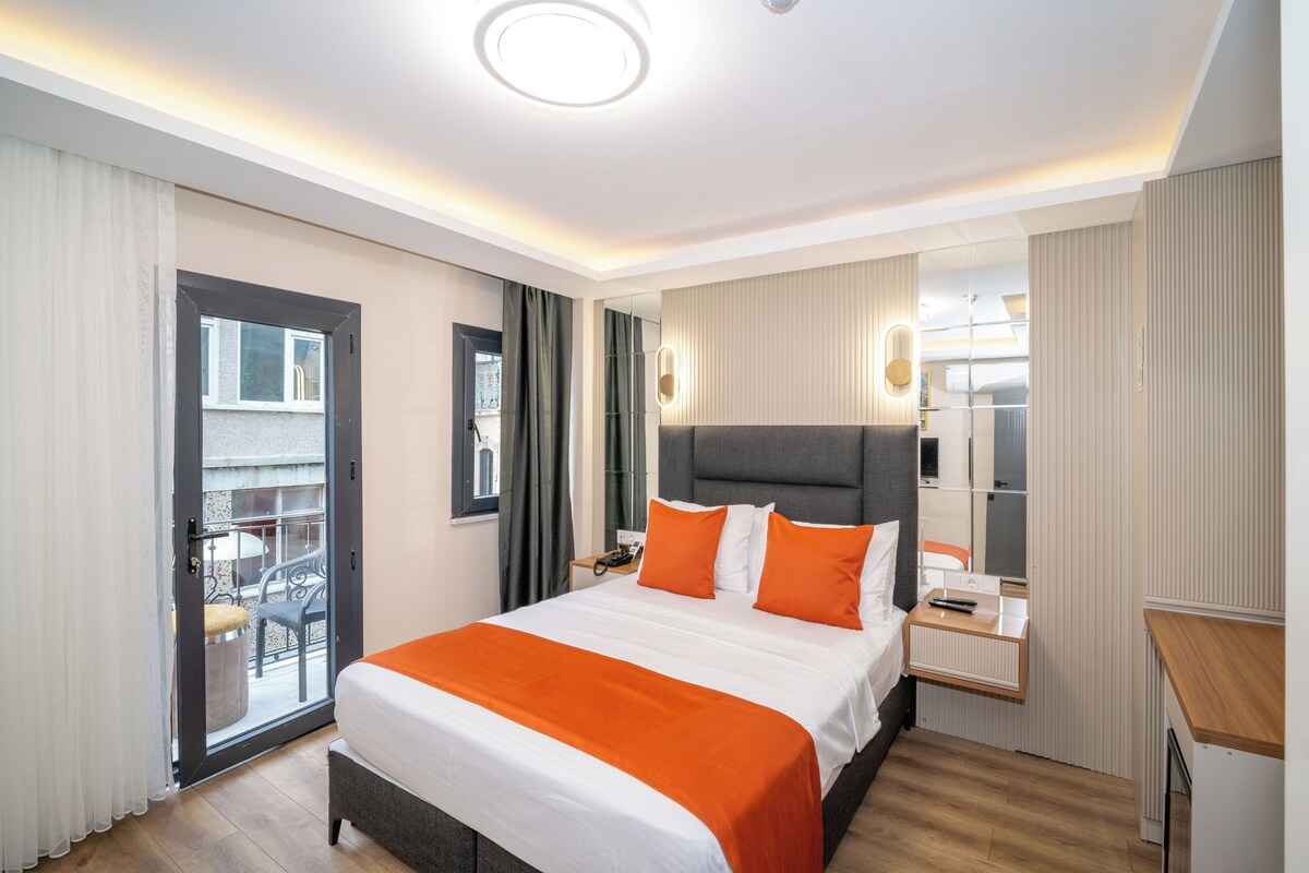 A modern hotel room with a large bed, a bedside table, a mirror, and a view of the outside balcony.