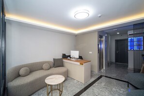 A reception area with a sofa, a small round table, a reception desk, and a corridor leading to an elevator. - Robin Hotel Istanbul (Istanbul)