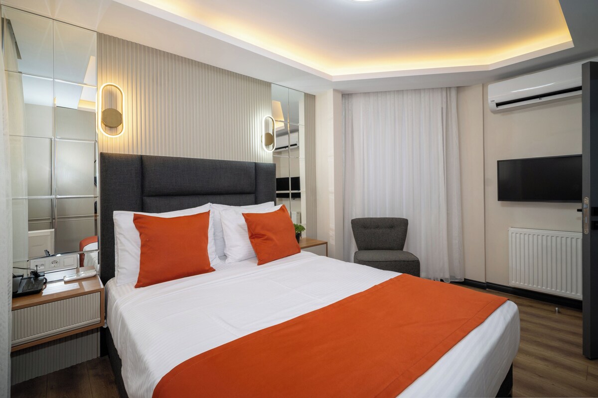 A hotel room with a large bed, a chair, a desk with a phone, a mirror, and a TV.