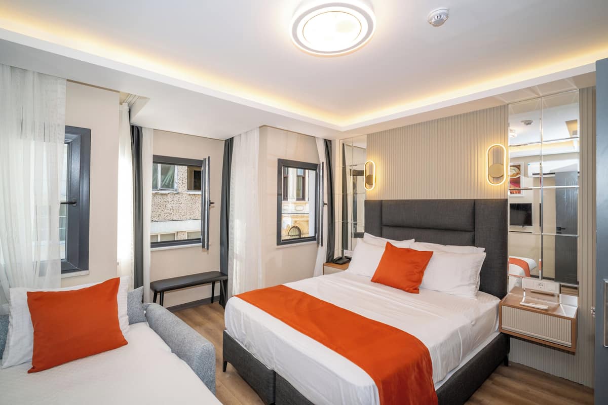 A hotel room with a bed, bedside table, mirror, and a view of the cityscape.