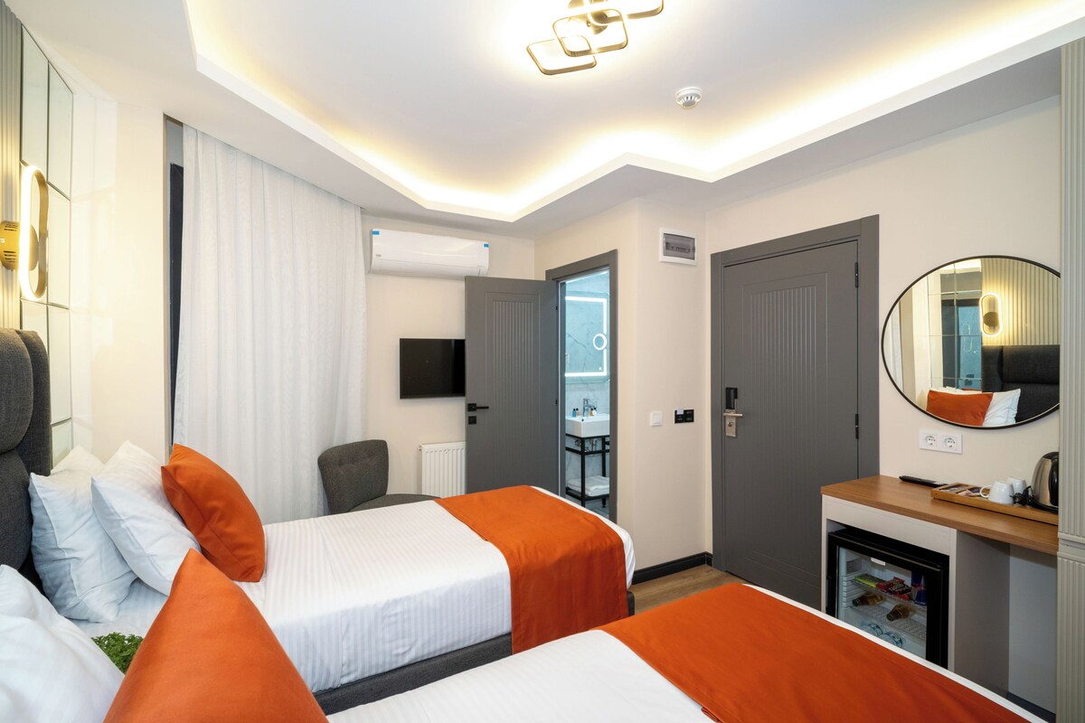 A hotel room with two beds, a desk with a refrigerator, a mirror, and a door leading to a bathroom.