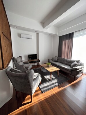Uma sala de estar moderna com um sofá, poltronas, uma mesa de centro e uma televisão.