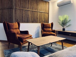 Ein modernes Wohnzimmer mit zwei braunen Ledersesseln, einem Holztisch, einem blauen Teppich und einer Blumentopf-Pflanze.