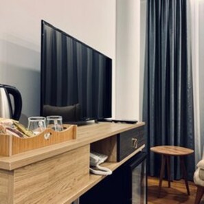 Ein modernes Hotelzimmer mit Schreibtisch aus Holz, einem Flachbildfernseher, einem Sessel und einem kleinen Hocker.