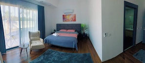 Ein Schlafzimmer mit einem Bett, einem Sessel, einem kleinen Tisch, einer Pflanze und einem Bild an der Wand.