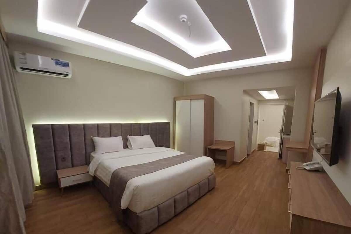 A modern hotel room with a large bed, a desk, a wardrobe, and a television.