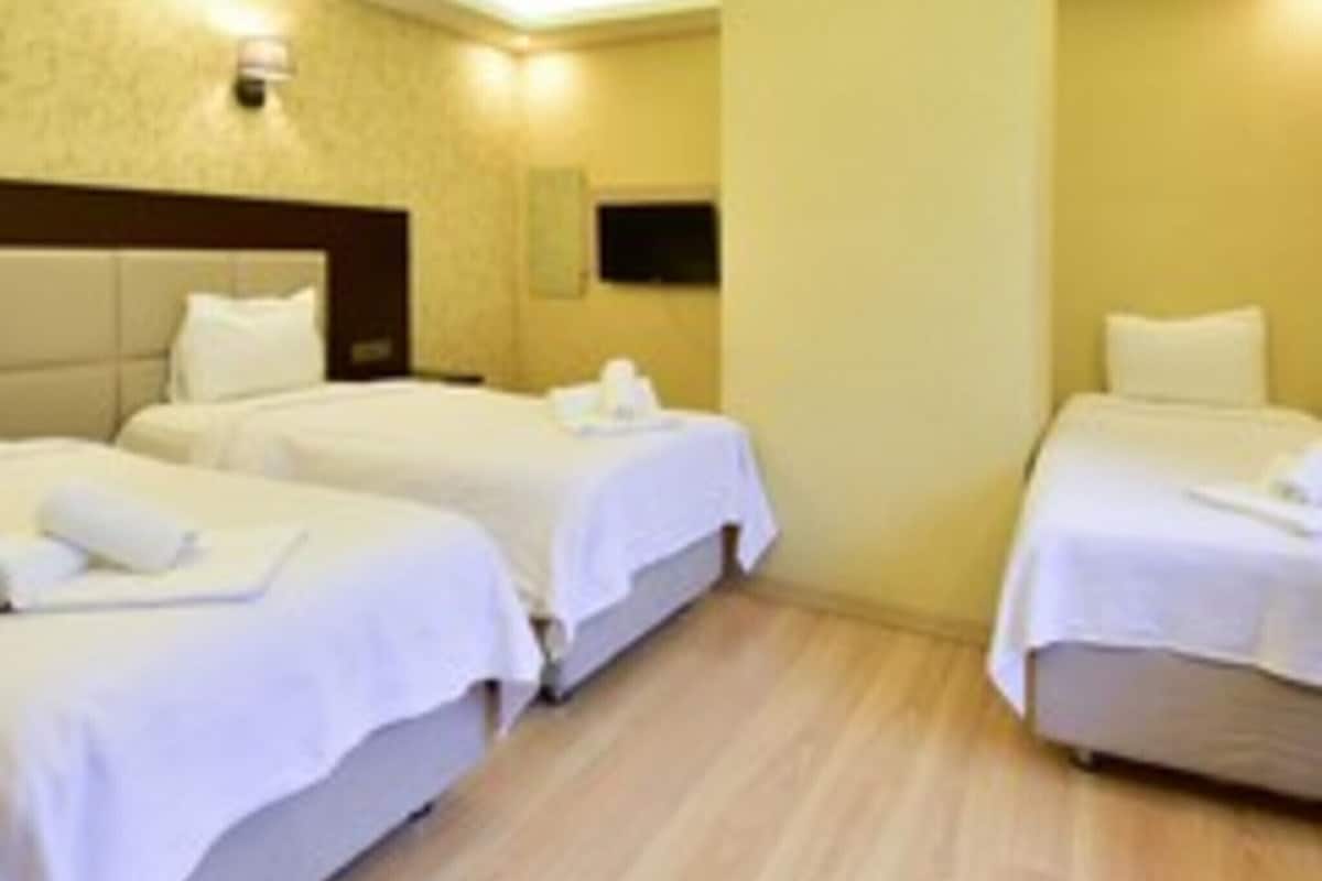 A hotel room with two single beds, a headboard, a wall-mounted light, and a wooden floor.