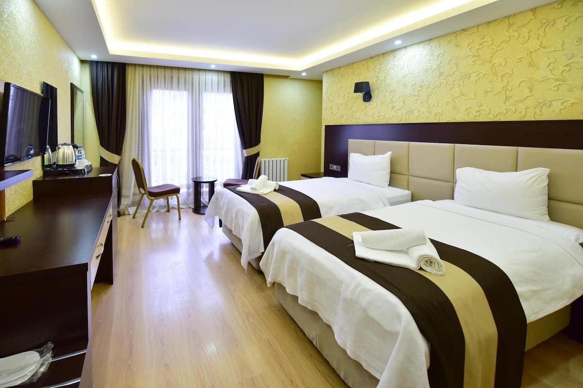 A hotel room with two beds, a desk with a TV, a chair, and a window with curtains.