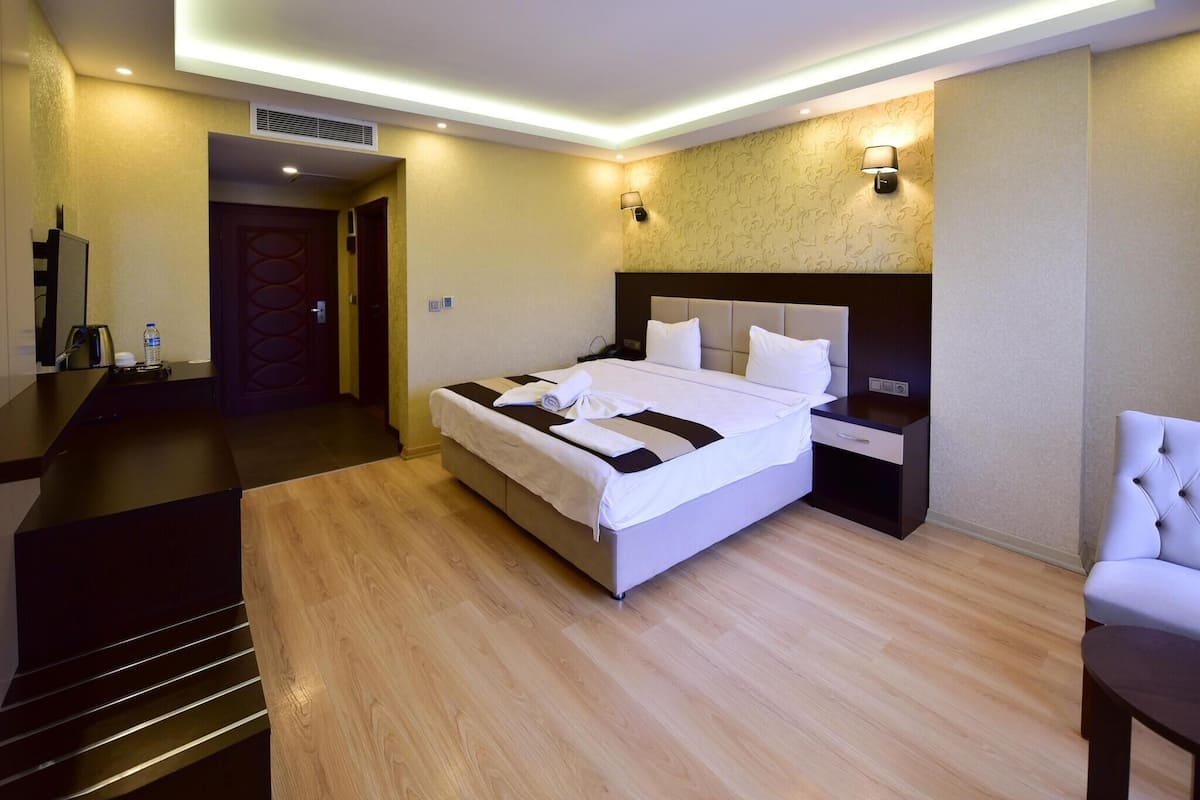 A modern hotel room with a large bed, bedside tables, a desk, a chair, and a TV.