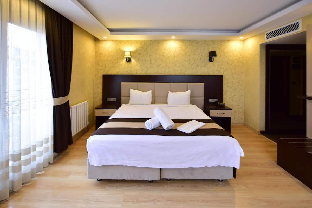 A hotel room with a large bed, two bedside tables, a headboard, and a window with curtains.