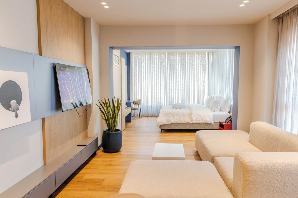 Ein modernes Hotelzimmer mit Bett, einer Sitzecke, einem an der Wand befestigten Fernseher und einer Zimmerpflanze.