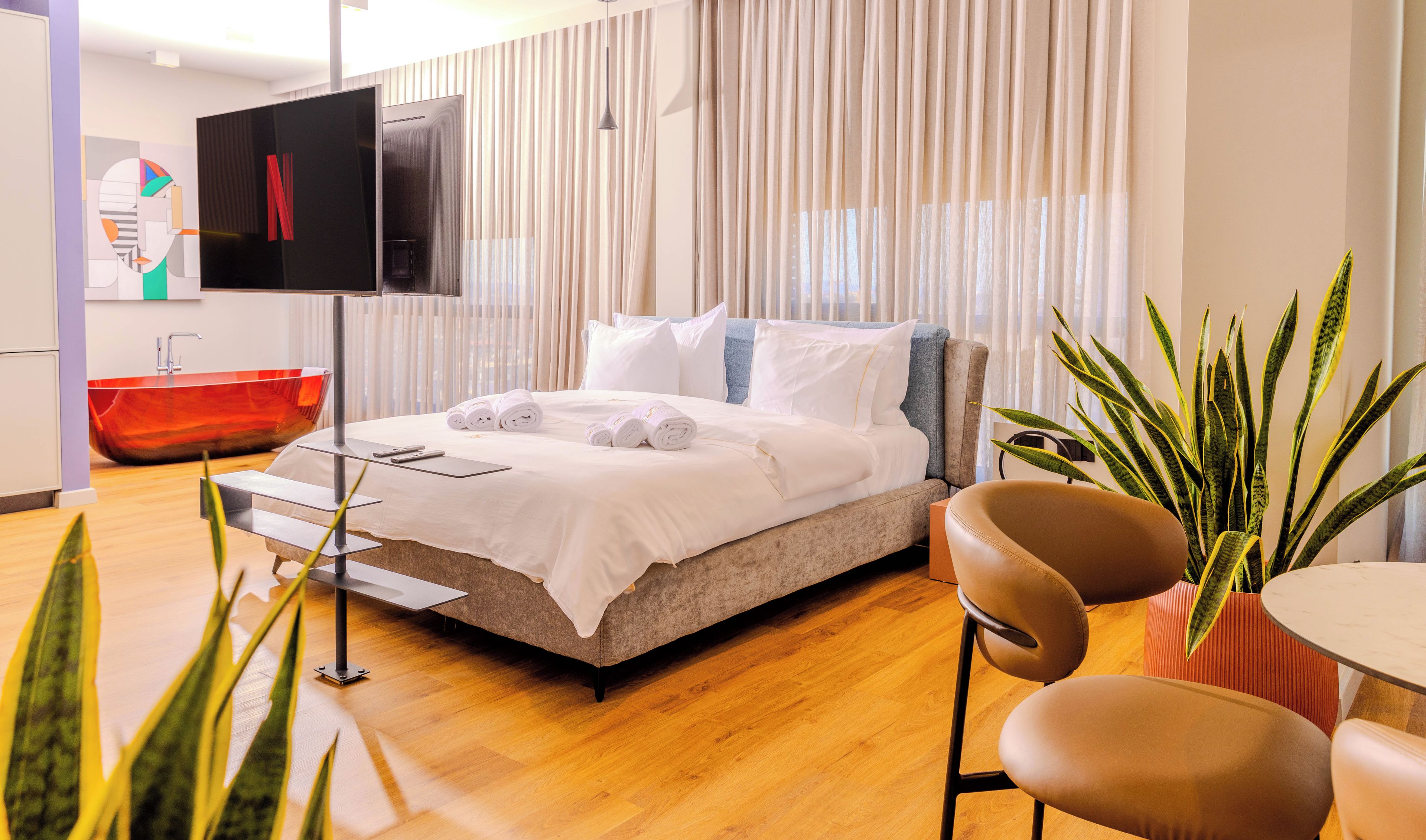 Una habitación de hotel moderna con cama, televisor, bañera roja y una planta en maceta.
