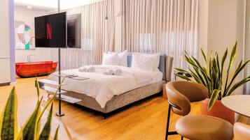 Una habitación de hotel moderna con cama, televisor, bañera roja y una planta en maceta.
