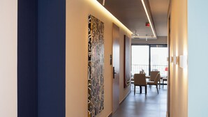 A modern hotel corridor with a blue accent wall, a patterned artwork, and a dining area with chairs and a table. - Si Hotel Sh.p.k (Tirana)