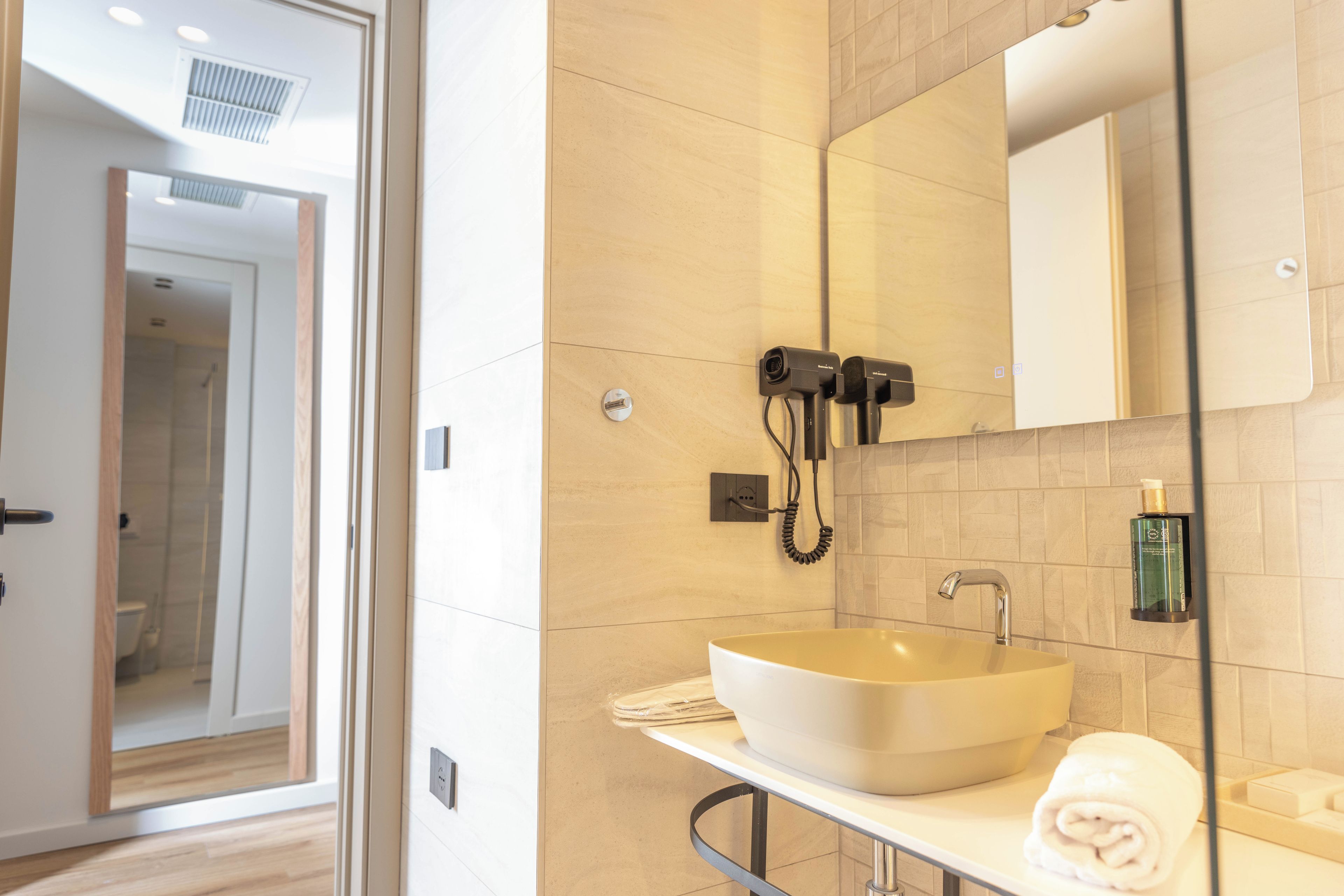 A modern bathroom with a large white sink, a mirror, and a hairdryer mounted on the wall.