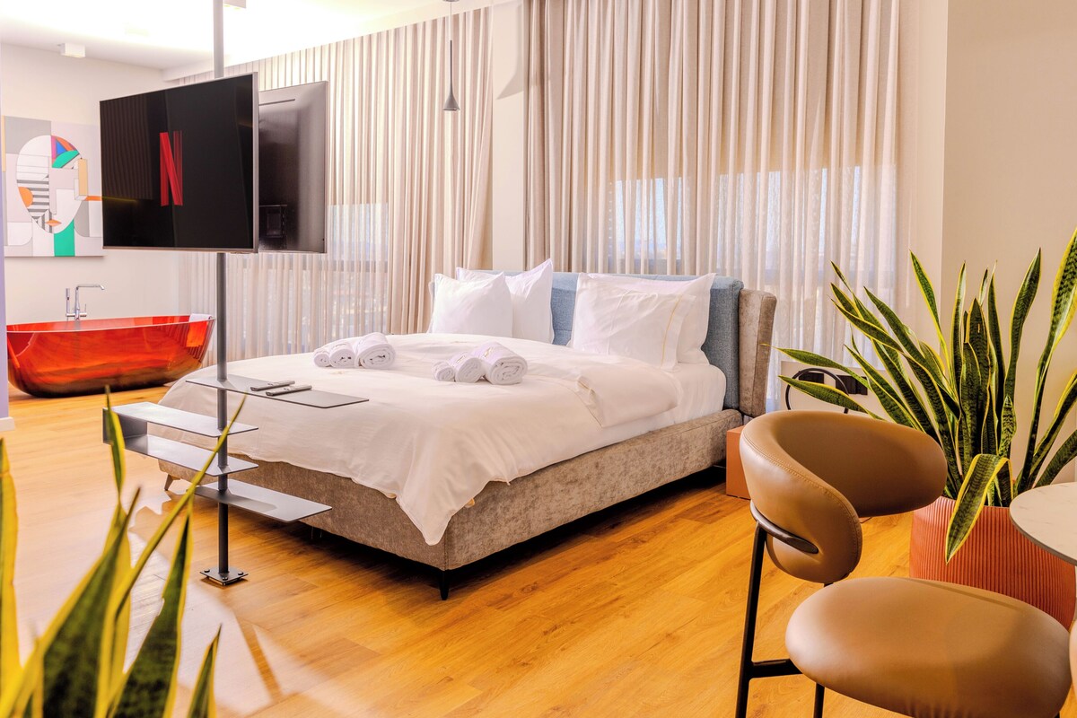 Ein modernes Hotelzimmer mit Bett, Fernseher, einer roten Badewanne und einer Topfpflanze.